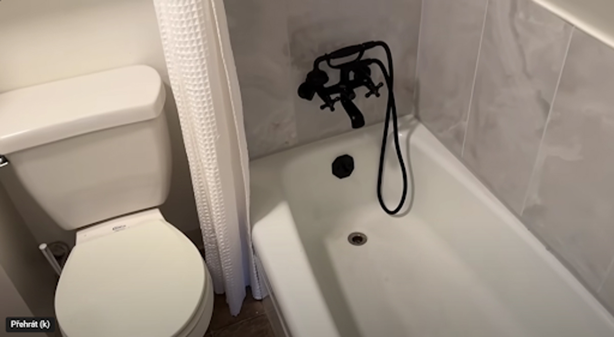 Malá koupelna s WC a vanou, černá baterie se sprchovou hadicí a bílý texturovaný závěs.