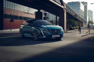 Peugeot 308 SW v jízdě moderním městem, zepředu s denním LED podpisem.