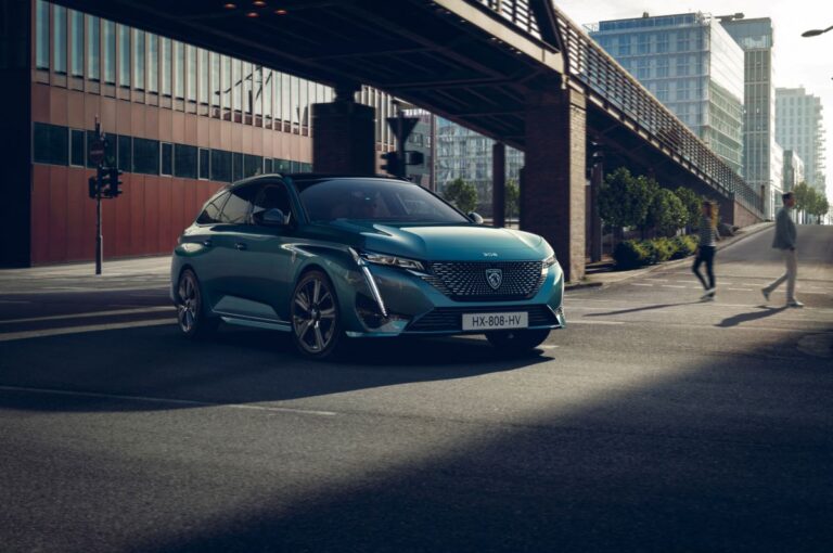 Peugeot 308 SW v jízdě moderním městem, zepředu s denním LED podpisem.