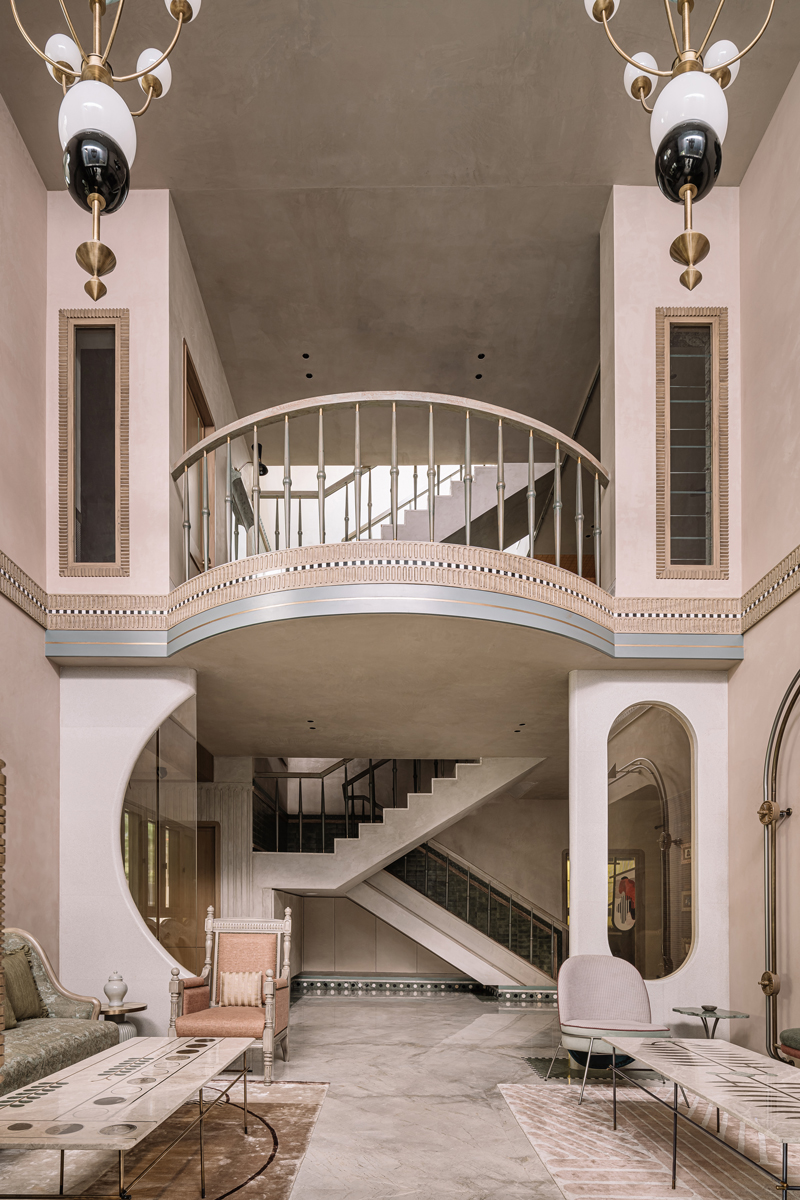 Široký záběr na galerii s obloukovým čelem, dekorativní lištování, schodiště s ostrou linií podesty, salon s historizujícími křesly a mramorovou podlahou v teplých pastelových barvách.