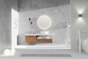 Elegantní koupelna s betonovými stěnami, moderním dřevěným umyvadlovým pultem a kruhovým podsvíceným zrcadlem.