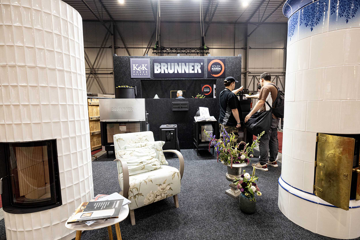 Expozice BRUNNER na veletrhu: kachlová kamna, krbové vložky a návštěvníci u stánku.