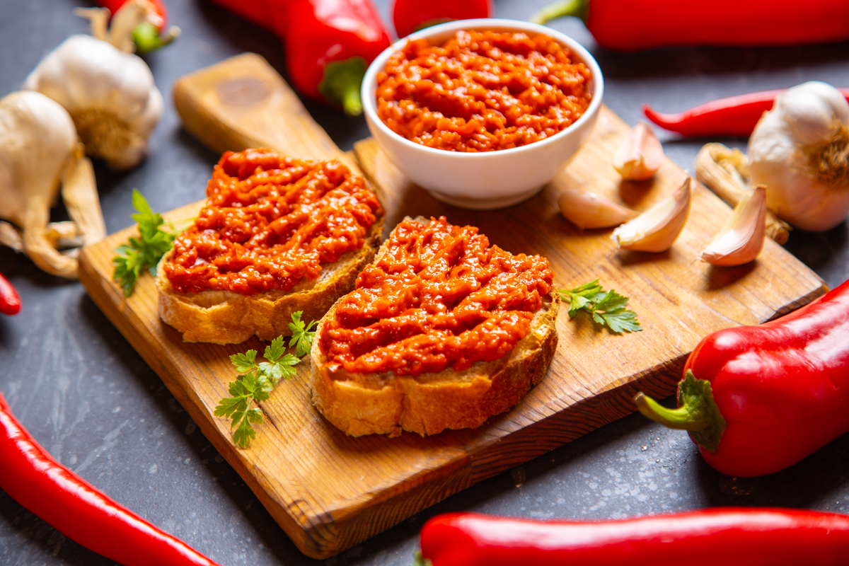Tradiční balkánský Ajvar z červených paprik podávaný na opečeném chlebu s česnekem a bylinkami.