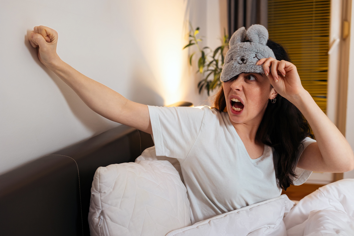 Žena v posteli bouchá na zeď kvůli hlučným sousedům.