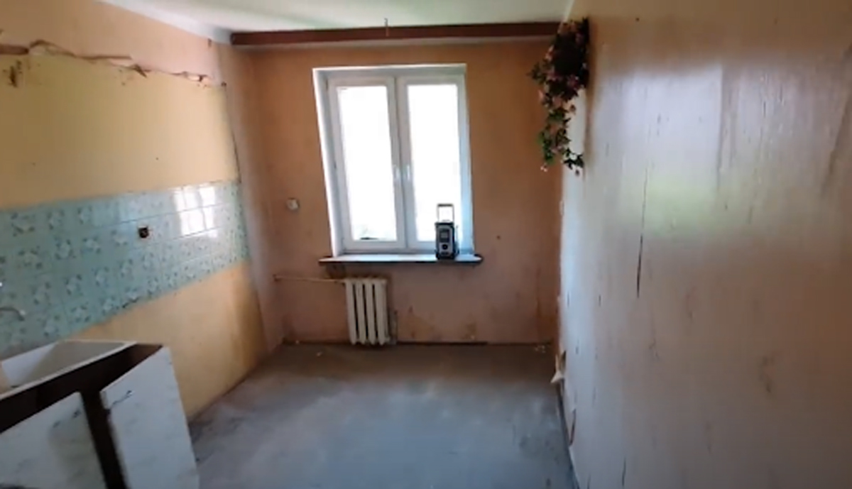 Kuchyň před rekonstrukcí s opotřebovaným obkladem a starým nábytkem.