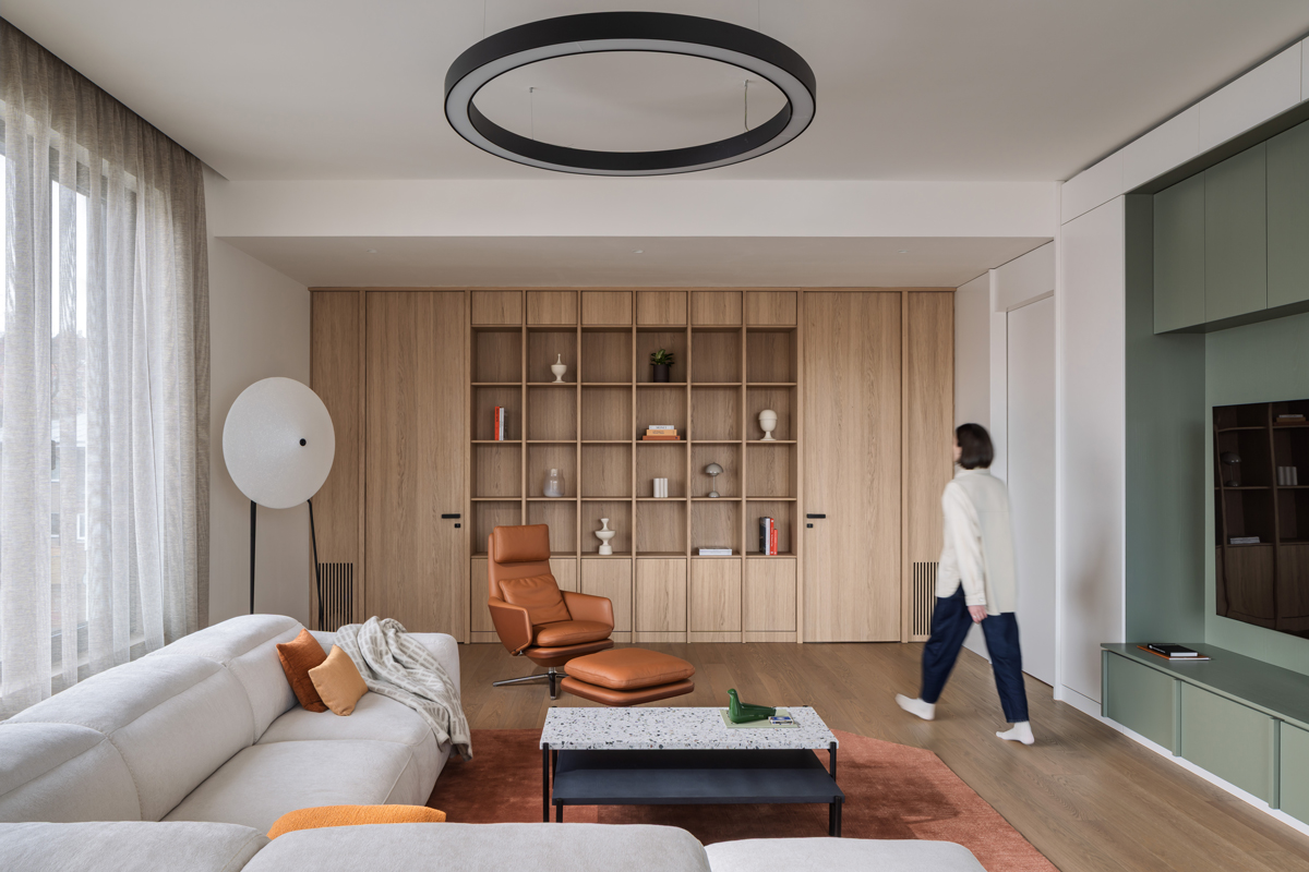 Prostorný obývací pokoj s velkou knihovnou, designovým křeslem a moderním osvětlením.