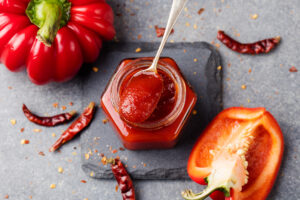 Domácí paprikový a chilli džem v malé sklenici s čerstvou i sušenou paprikou kolem.