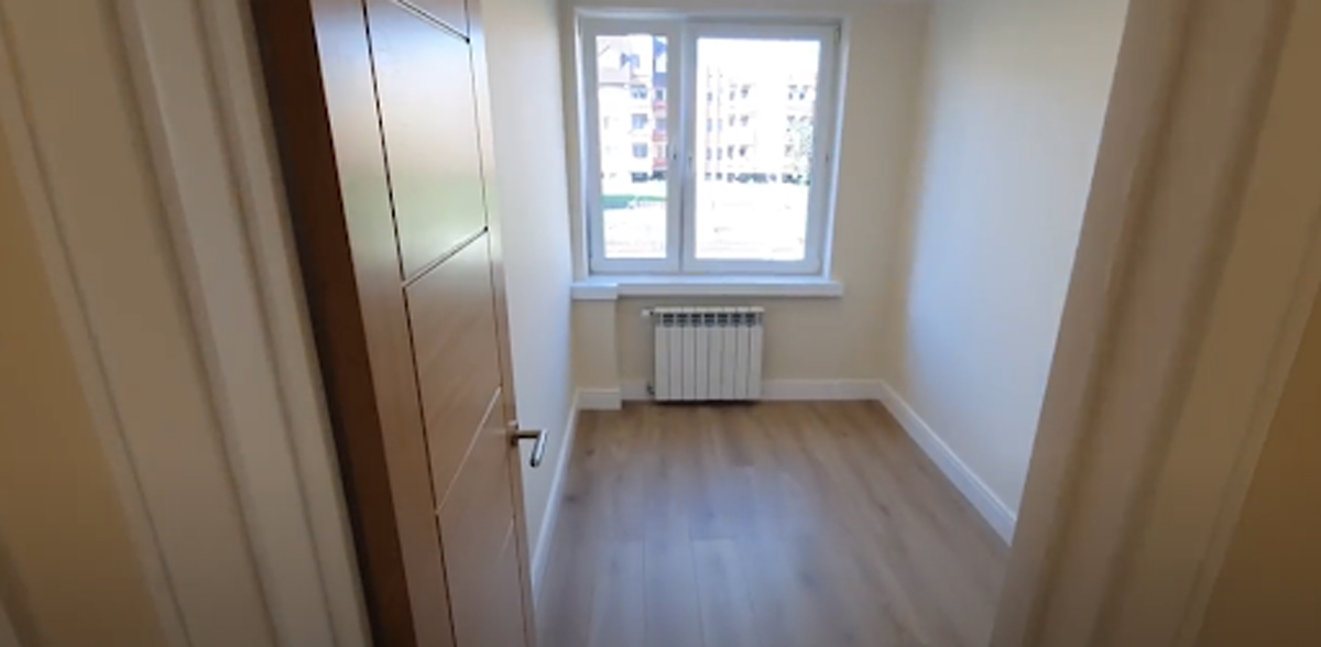 Světlý a minimalistický pokoj po rekonstrukci s novou podlahou a bílými stěnami.