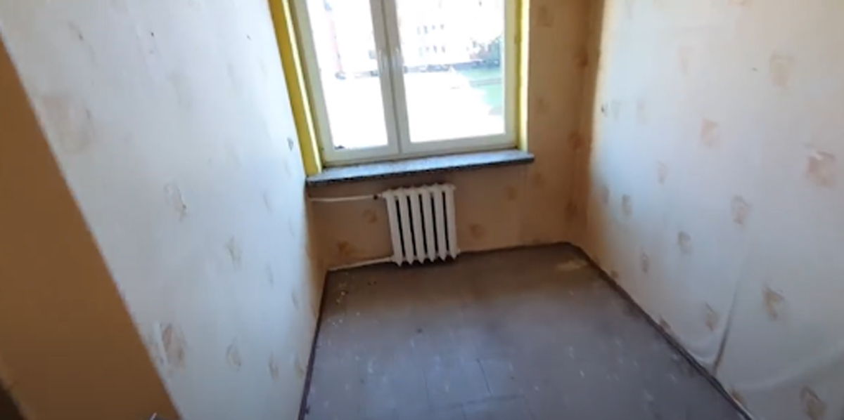 Malý pokoj před rekonstrukcí s původní podlahou a opotřebovanými radiátory.