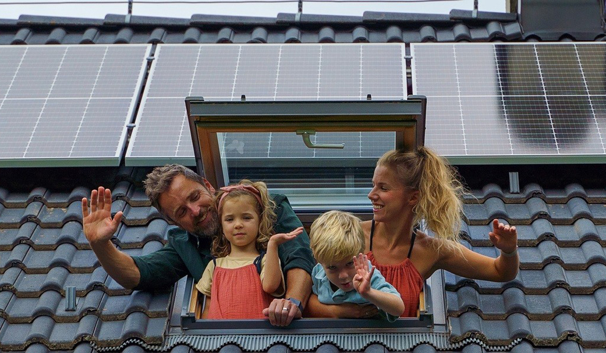 Rodina mává ze střešního okna domu se solárními panely na taškové střeše.
