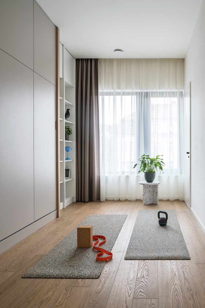 Moderní domácí cvičební kout s podložkami, cvičebními pomůckami a velkým oknem se záclonami, který působí svěže a motivuje k relaxaci i tréninku.