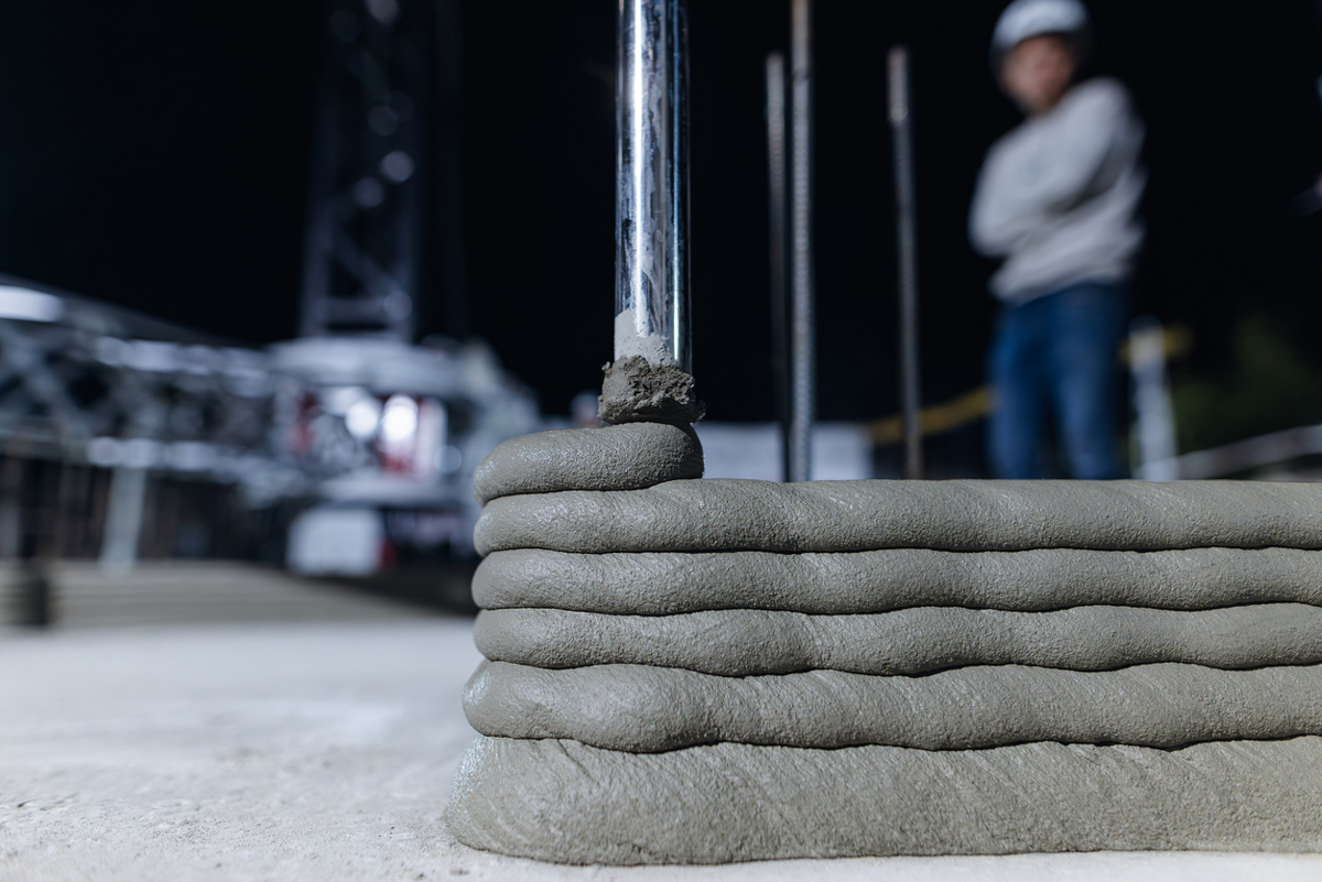 Robotická tryska nanášející beton při 3D tisku zdi domu, moderní stavební technologie v praxi.