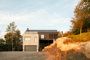 Moderní dům s tmavou střechou zasazený do skalnatého svahu, nasvícený teplým podvečerním světlem.