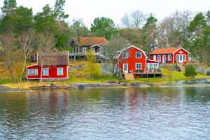 Skupina typických červených dřevěných chatek na skalnatém břehu švédského jezera.