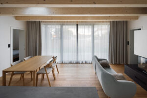 Interiér denní zóny s dřevěným nábytkem, velkými okny a neutrální barevností v domě v Křenovicích.