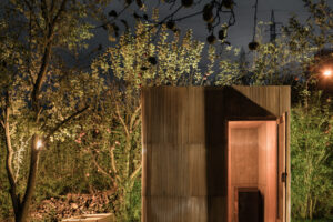 Malá dřevěná sauna z europalet a sklolaminátu zasazená do přírodní zahrady.