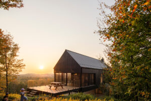 Moderní dřevěný dům na vyvýšené terase obklopený lesem při západu slunce.