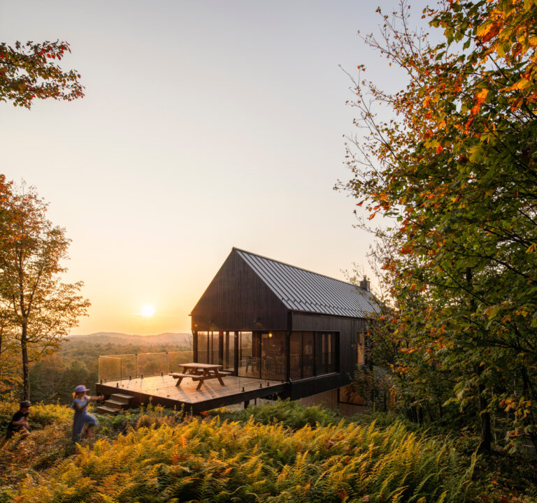 Moderní dřevěný dům na vyvýšené terase obklopený lesem při západu slunce.