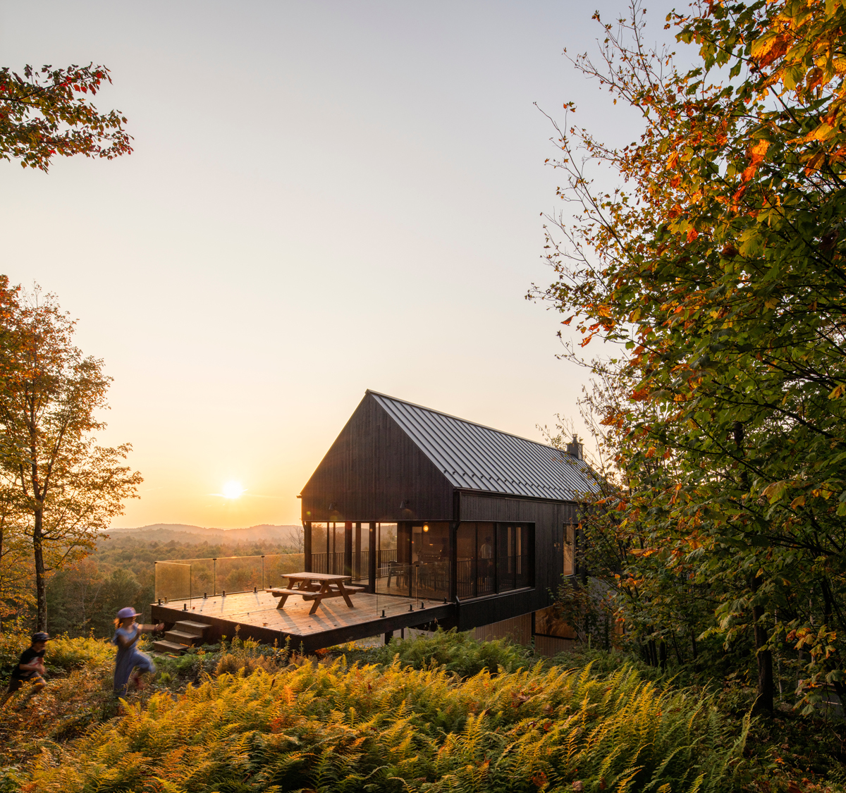 Moderní dřevěný dům na vyvýšené terase obklopený lesem při západu slunce.