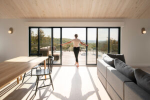 Světlý obývací prostor s dřevěným stropem a posuvnými skleněnými dveřmi na terasu s panoramatickým výhledem.