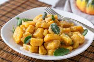 Domácí dýňové gnocchi s máslem, šalvějí a parmazánem na bílém talíři.
