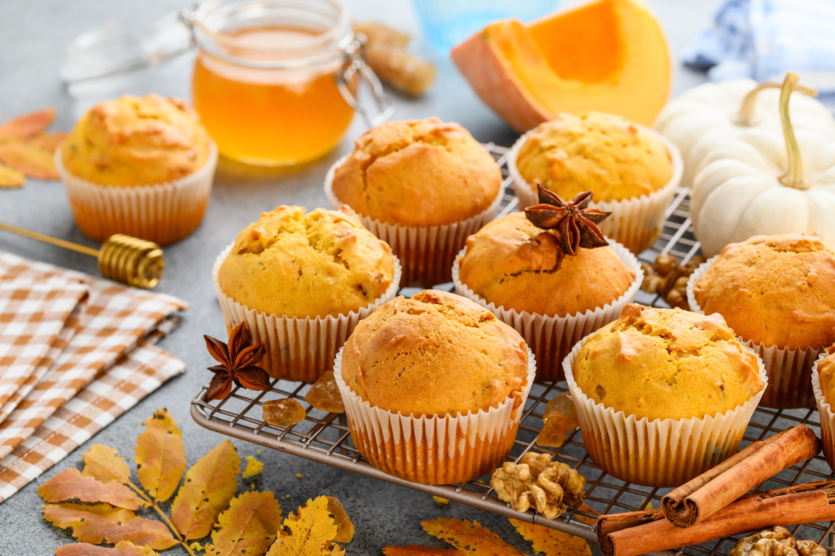Dýňové muffiny se skořicí a ořechy na chladicí mřížce, obklopené podzimní dekorací.