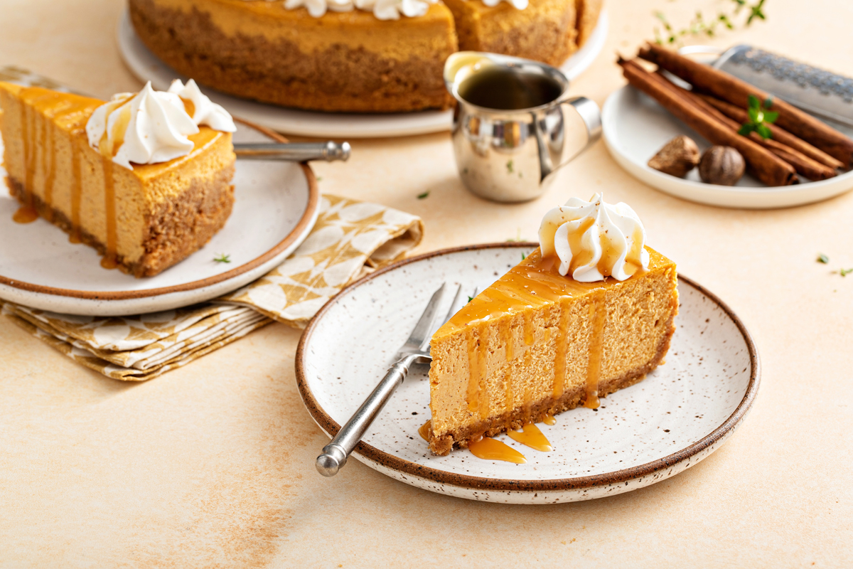 Dýňový cheesecake s karamelovou polevou a šlehačkou na talíři, doplněný skořicí a muškátovým oříškem.