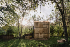 Venkovní sauna z recyklovaných materiálů s přírodní izolací z ovčí vlny uprostřed městské zahrady.