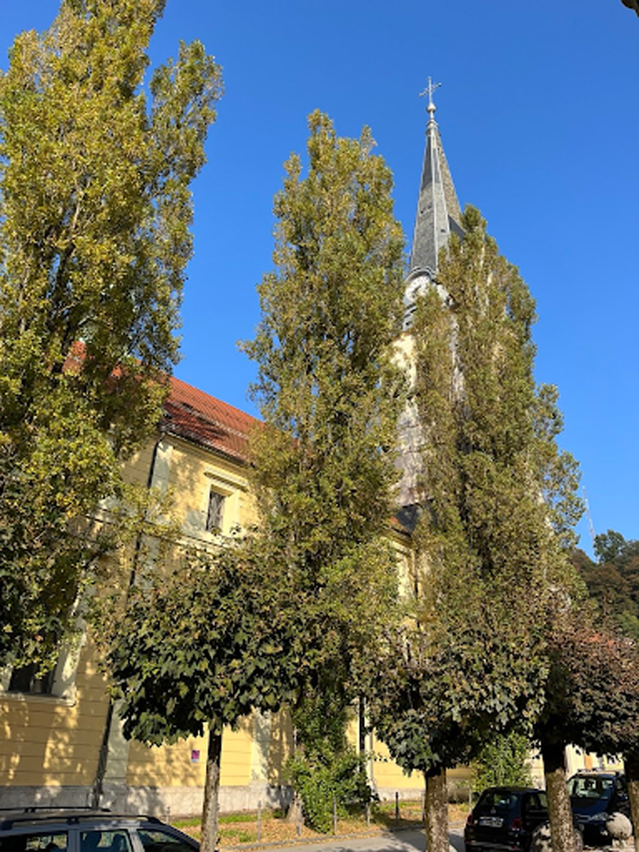 Kostel sv. Jakuba v Lublani obklopený stromy s vysokou věží.