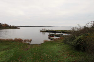 Malé dřevěné loďky zakotvené u břehu jezera obklopeného podzimní přírodou.