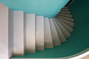 Křivkové točité schodiště s tyrkysovou stěnou, zachycené shora v moderním domě v Křenovicích.