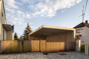 Vstupní branka a dřevěné oplocení s betonovým přístřeškem u rodinného domu v Křenovicích.