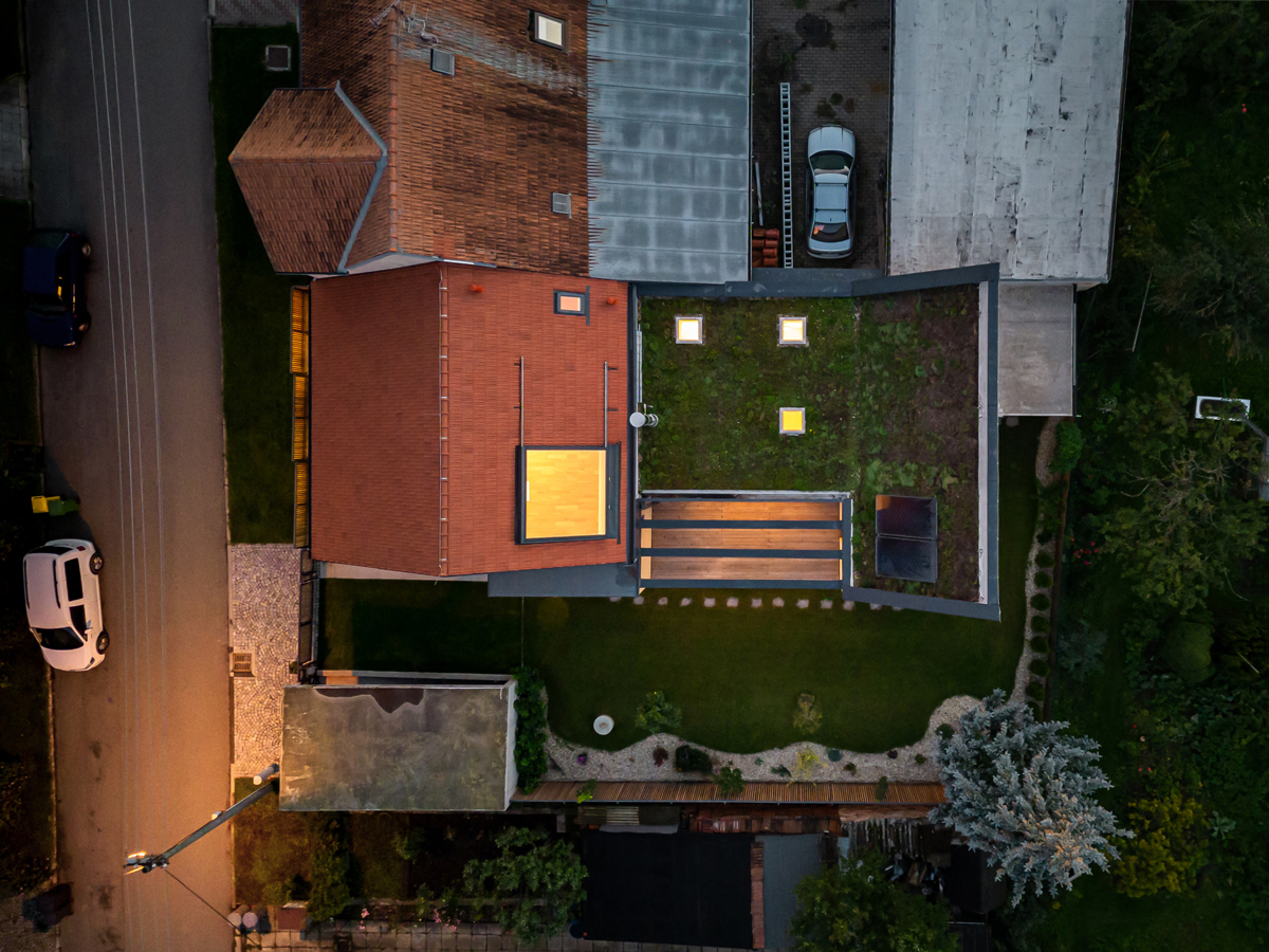 Noční letecký pohled na dům v Křenovicích se zelenou střechou a prosvětlenou přístavbou.