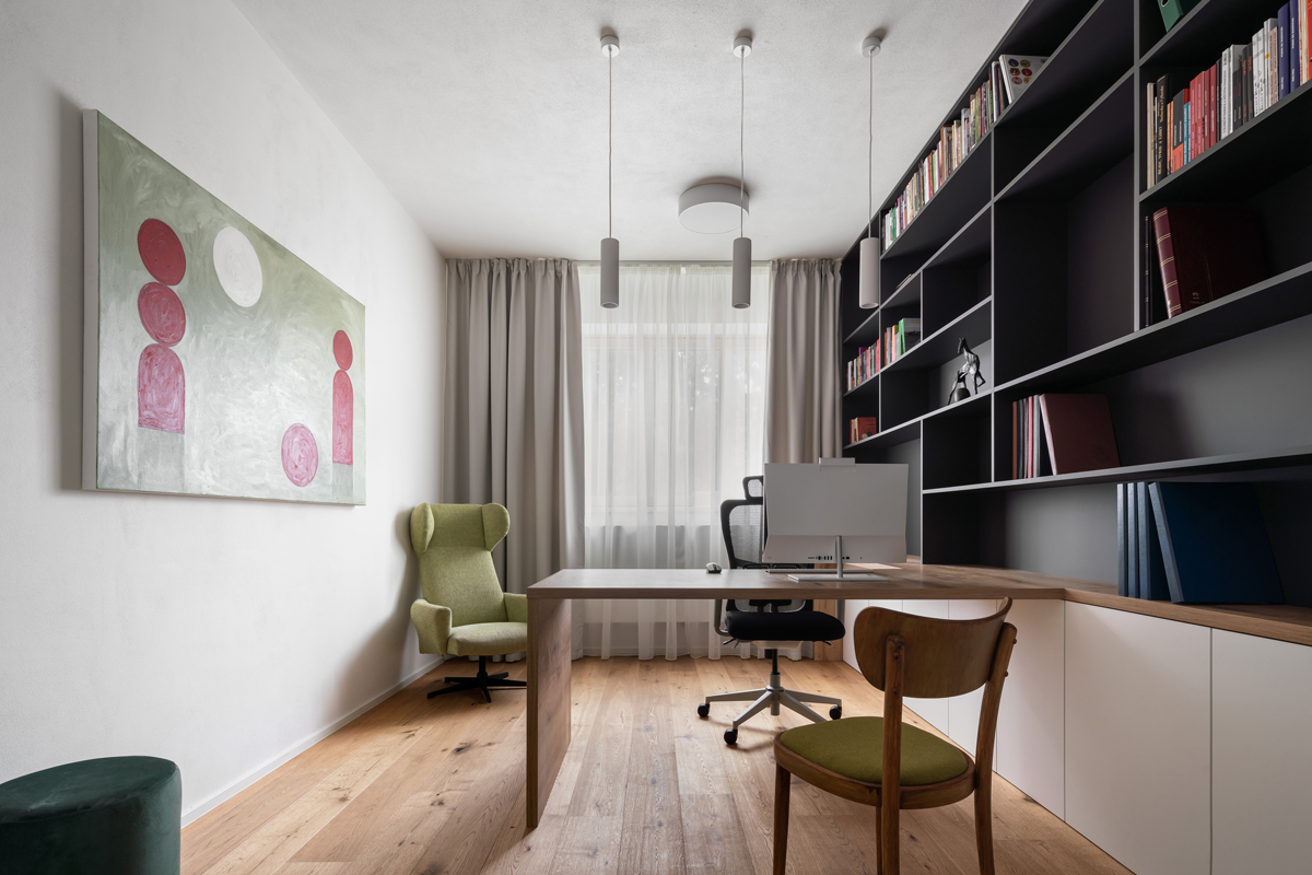 Moderní pracovna s dřevěnou podlahou, policemi na knihy a zeleným křeslem v rodinném domě v Křenovicích.