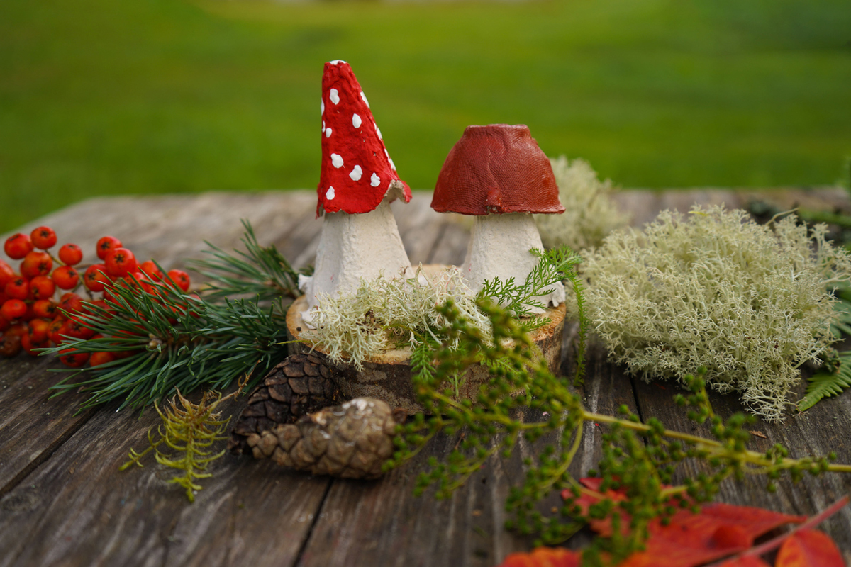 Přírodní dekorace s ručně vyrobenými houbičkami, mechem, jehličím a jeřabinami na dřevěném stole.
