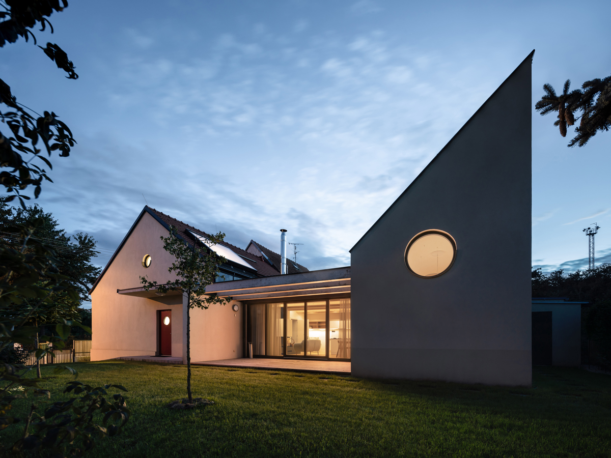 Osvětlený rodinný dům v Křenovicích při soumraku, s prosklenou fasádou a zelenou střechou.
