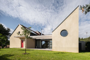 Pohled na zadní část rodinného domu v Křenovicích se zelenou střechou a prosklenou fasádou směrem do zahrady.