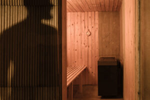 Pohled do interiéru sauny obložené smrkovými deskami s kamny a lavicí v teplém světle.