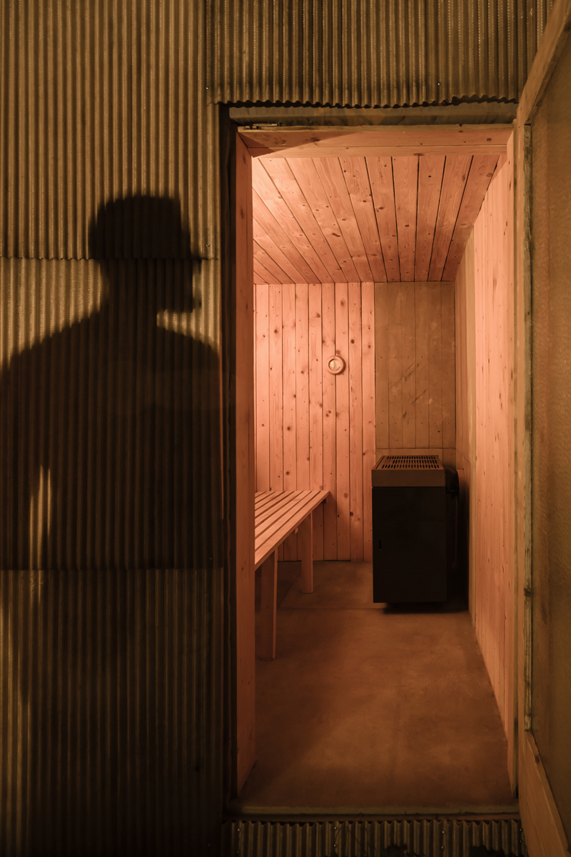 Pohled do interiéru sauny obložené smrkovými deskami s kamny a lavicí v teplém světle.