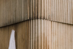 Detail fasády venkovní sauny z vlnitého sklolaminátu s jemnými stopami používání a zavěšeným ručníkem.