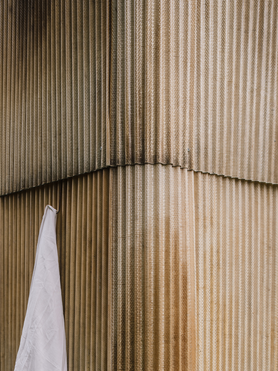 Detail fasády venkovní sauny z vlnitého sklolaminátu s jemnými stopami používání a zavěšeným ručníkem.