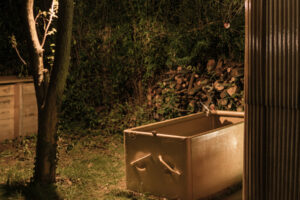 Noční záběr ochlazovací vany u sauny postavené z europalet a sklolaminátu, nasvícené teplým světlem.