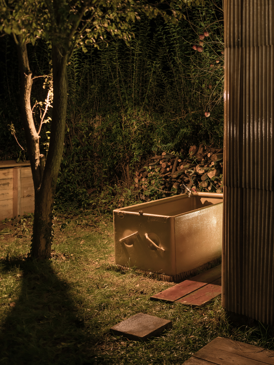 Noční záběr ochlazovací vany u sauny postavené z europalet a sklolaminátu, nasvícené teplým světlem.