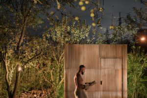 Venkovní sauna z recyklovaných materiálů a vana na ochlazení, nasvícené nočními světly mezi stromy.