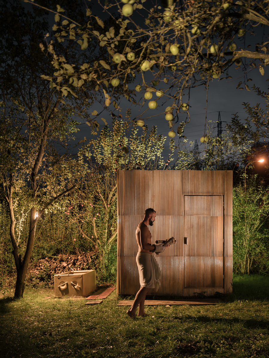 Venkovní sauna z recyklovaných materiálů a vana na ochlazení, nasvícené nočními světly mezi stromy.