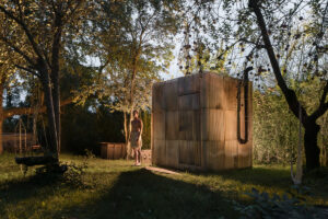 Celkový pohled na venkovní saunu z europalet, ovčí vlny a sklolaminátu, nasvícenou teplým večerním světlem.