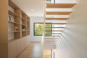 Minimalistické interiérové schodiště z dubového dřeva, doplněné vestavěnou knihovnou a výhledem do přírody.