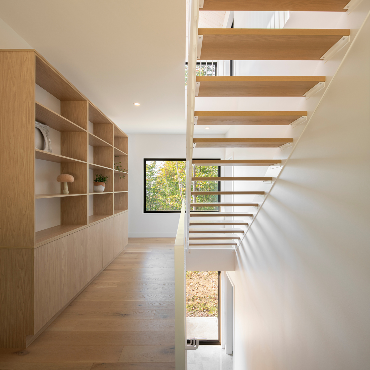 Minimalistické interiérové schodiště z dubového dřeva, doplněné vestavěnou knihovnou a výhledem do přírody.