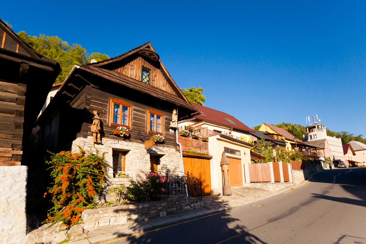 Historická roubená chalupa ve Štramberku s květinovými truhlíky a zděným přízemím.