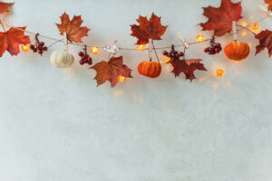 Ručně vyráběná podzimní dekorace z listů, malých dýní a světýlek zavěšená na provázku.